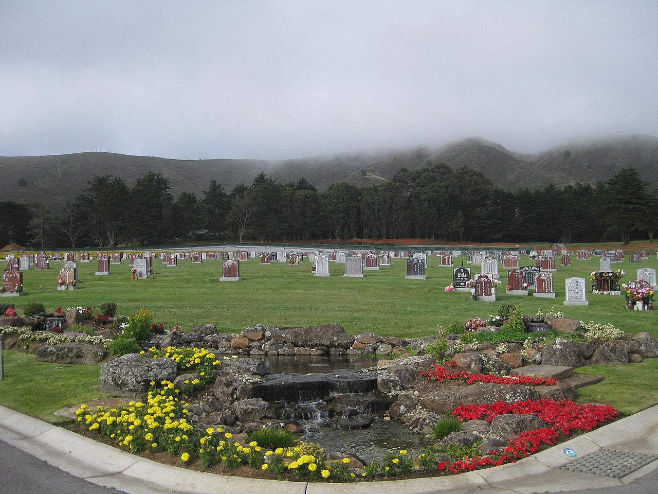 Cypress Lawn Memorial Park grounds in Colma with graves, trees, flowers and the San Bruno Mountain hillside