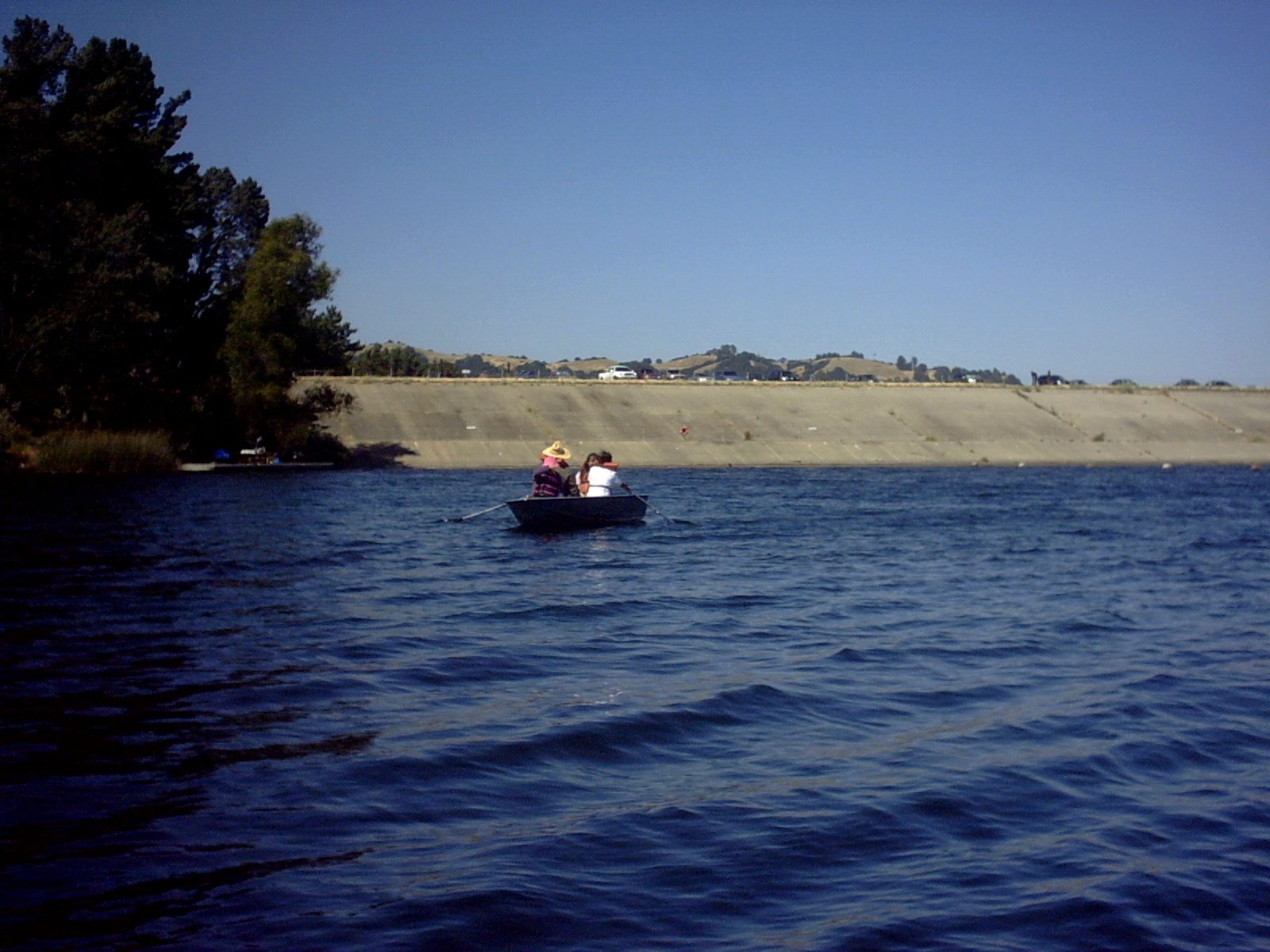 A small boat on the blue water of Lafayette Reservoir with wooded hills behind